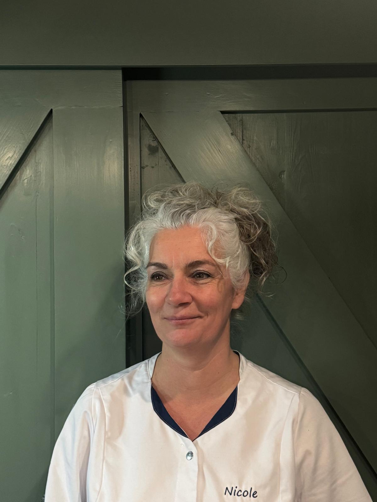 Nicole Geujen in haar witte werkjasje voor een groene deur